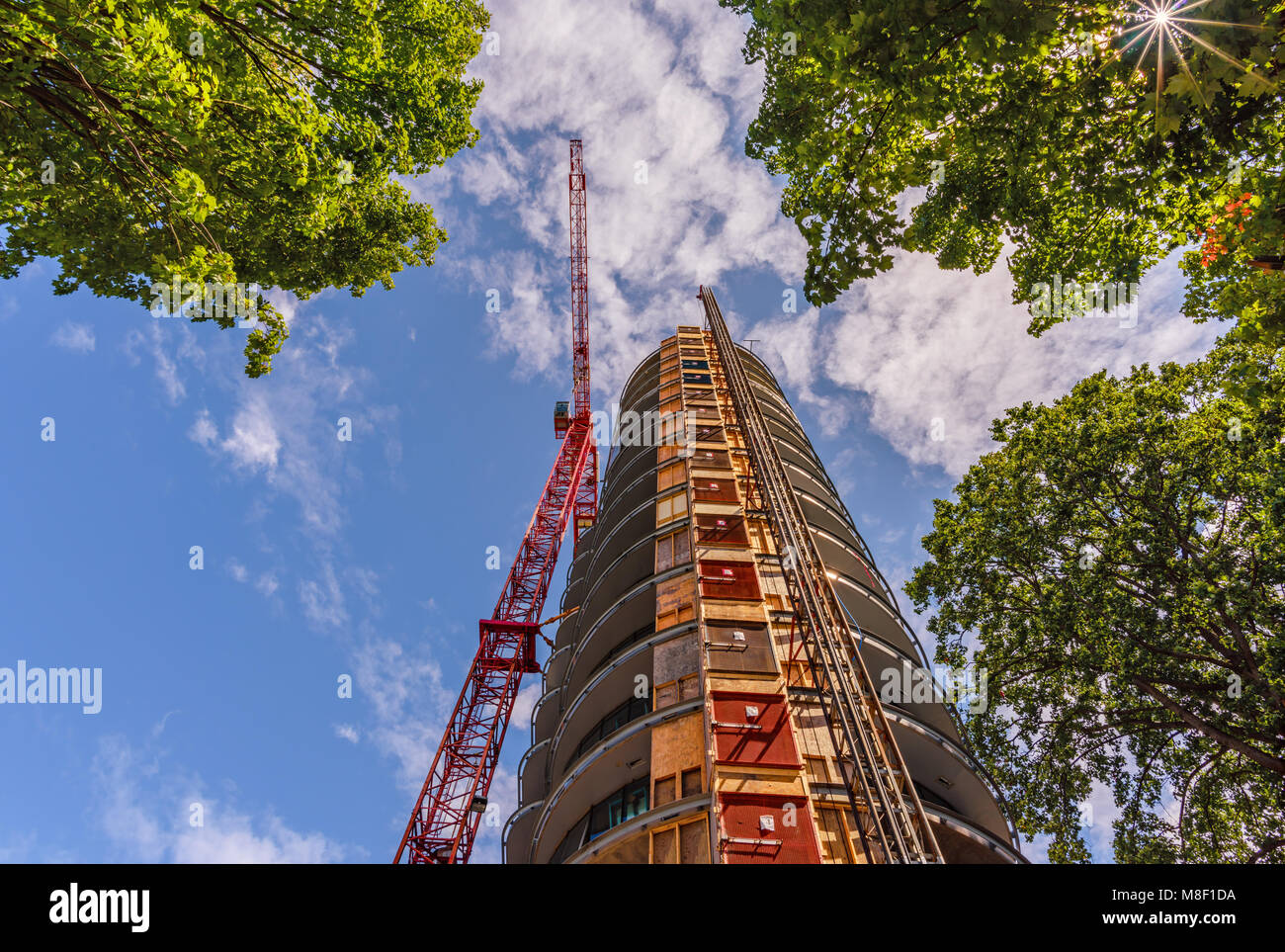 Vista dal basso verso l'alto sulla costruzione di una gru a torre, un edificio a più piani in un giorno di estate contro un cielo blu e nuvole bianche Foto Stock