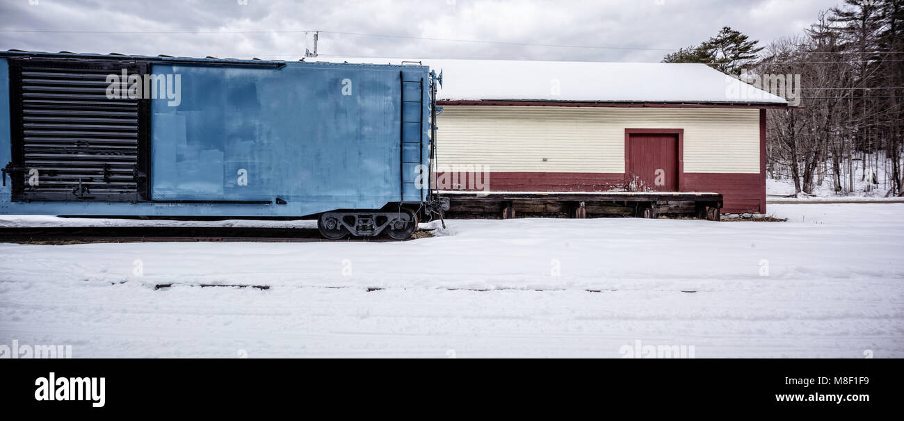 Un vintage vecchia stazione box auto parcheggiate in una schierata accanto a una vecchia casa del trasporto merci nella neve. Foto Stock