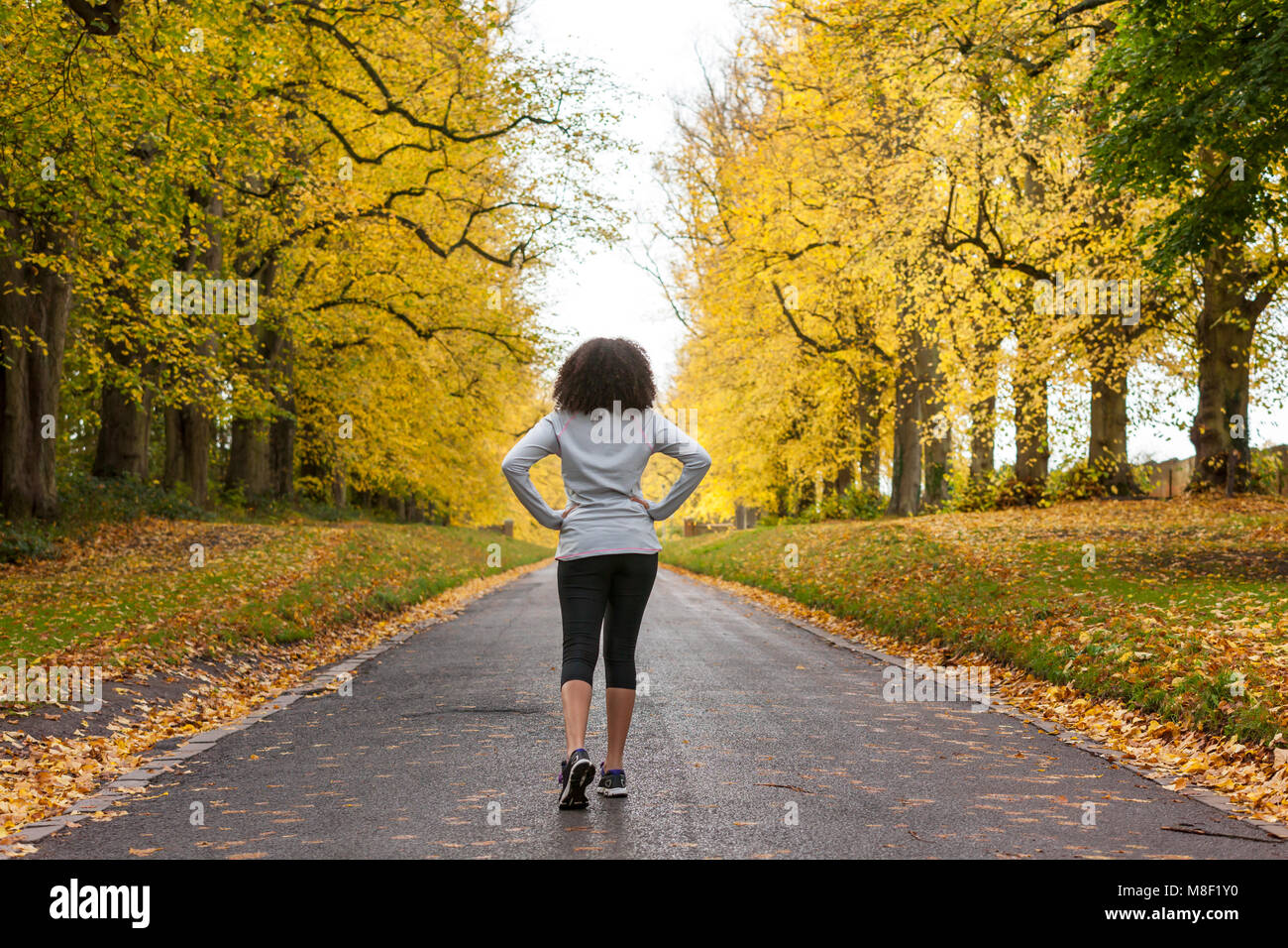 Bellissima gara di misto americano africano donna giovane ragazza adolescente preparando per il fitness in esecuzione jogging sulla strada di Autunno Autunno alberi Foto Stock