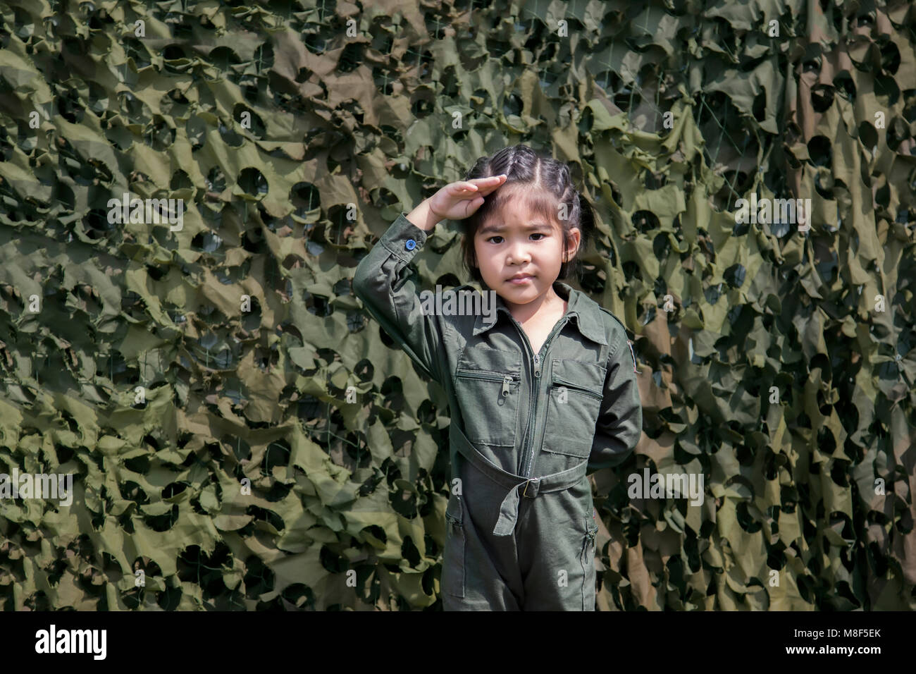 Ragazza asiatica rispetto soldato con azione soldato verde o pilota uniforme su una texture verde net sfondo bunker Foto Stock