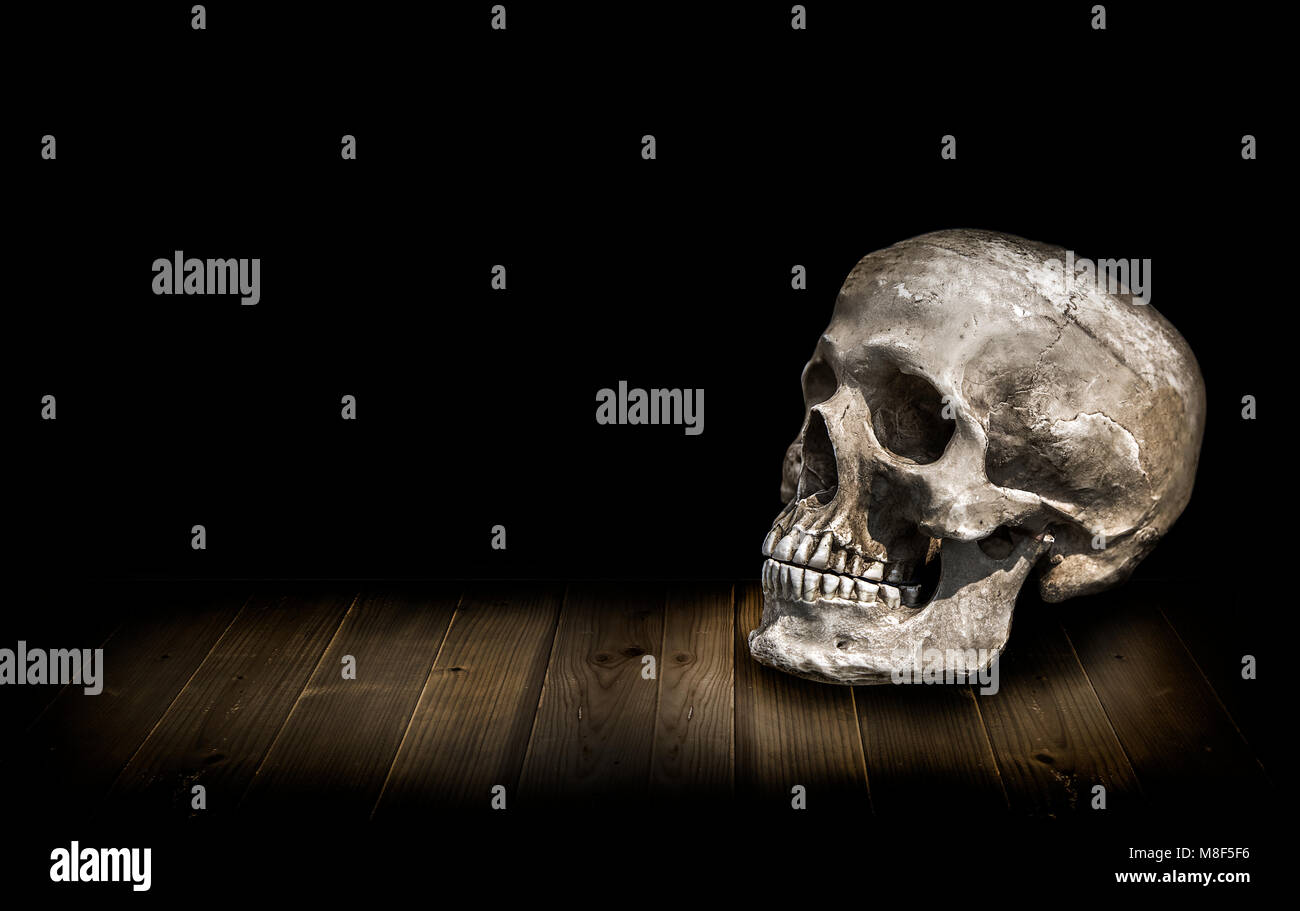 Scull umana sulla tavola di legno di sommità e di fondo nero essere un display storia di inquietante Ghost concetto con spazio di copia Foto Stock