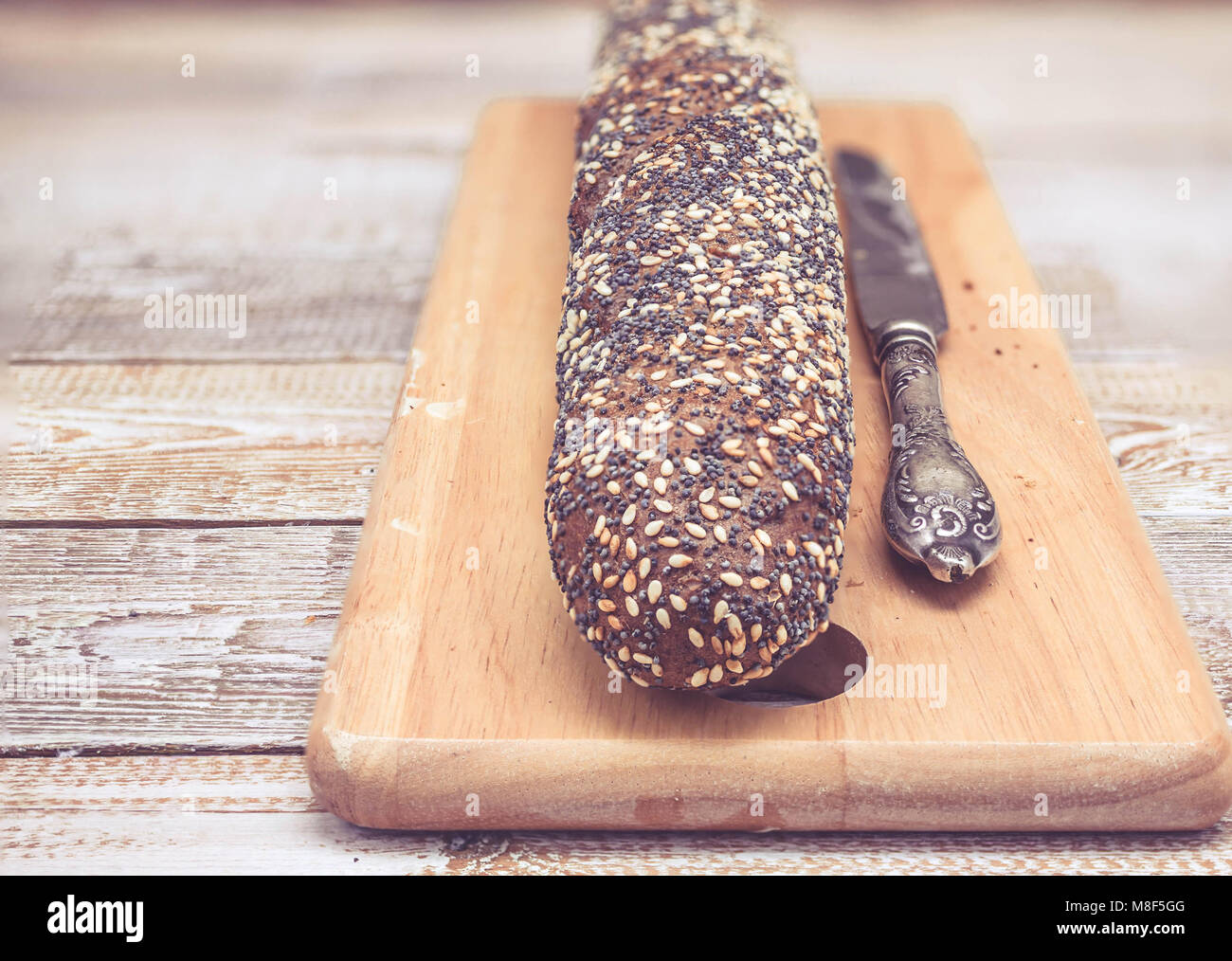 Pane di segale con semi di canapa e di un kino. Pane sano. Baguette e un coltello da tavola su un tagliere. Chiusa - Alto Foto Stock