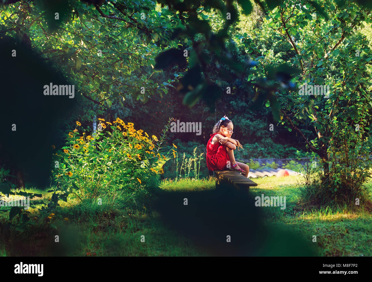 Bellezza ragazza romantica all'esterno. Bellissimo modello Teenage ragazza in abito rosso è seduta sul giardino nella luce del sole. Soffiando i capelli lunghi. L'estate. Glow Sun, S Foto Stock