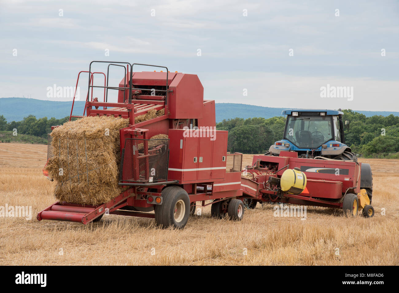 Un trattore rosso e il fieno depositante a sedersi in un campo di fieno alla fine del lavoro daay in una fattoria nella campagna del Maryland. Le montagne Catoctin sono in background. Foto Stock