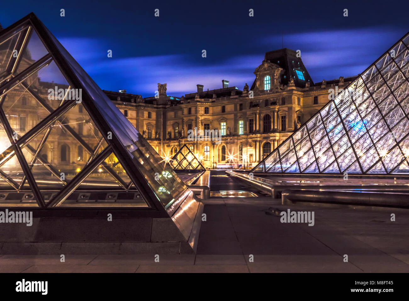Illuminato piramidi di vetro all'ingresso del museo del Louvre a Parigi con illuminazione atmosferica e cielo incandescente Foto Stock