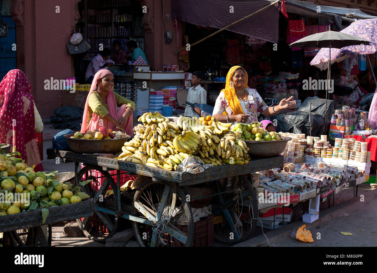 I mercanti di sesso femminile di vendita sono cresciuto in casa produrre a torre con orologio mercato di Jodhpur, India durante il giorno caldo e soleggiato. Le donne sono sorridente, indossando variopinti dre Foto Stock