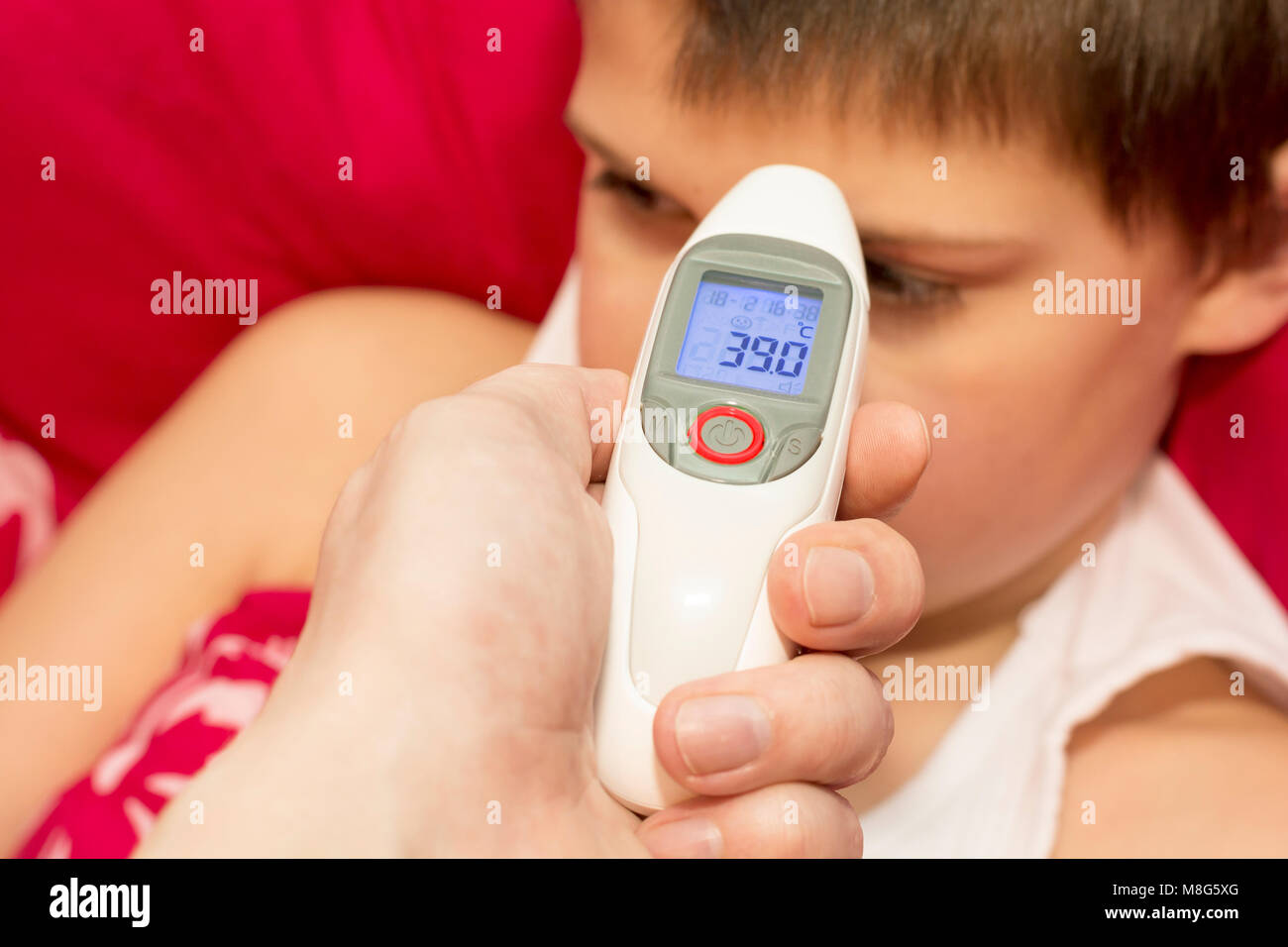 Misurazione della temperatura sul fronte in non-termometro a contatto. La stagione influenzale. Dormire ragazzo malato con la temperatura. In appoggio sulla malattia. Foto Stock