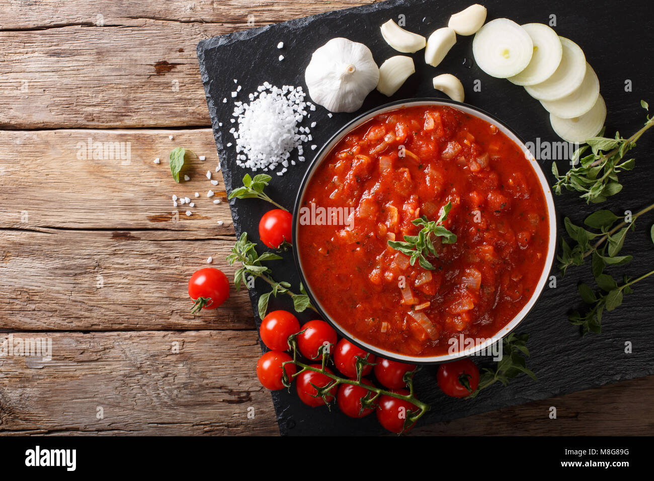 Italiano salsa pizzaiola con pomodori, origano e aglio e cipolla vicino sul tavolo. parte superiore orizzontale vista da sopra Foto Stock