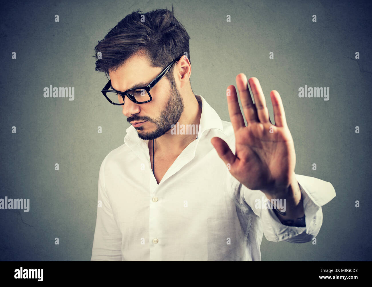Infastiditi triste uomo dando parlare a mano gesto isolato su sfondo grigio. Emozione negativa faccia sensazione di espressione del linguaggio del corpo Foto Stock
