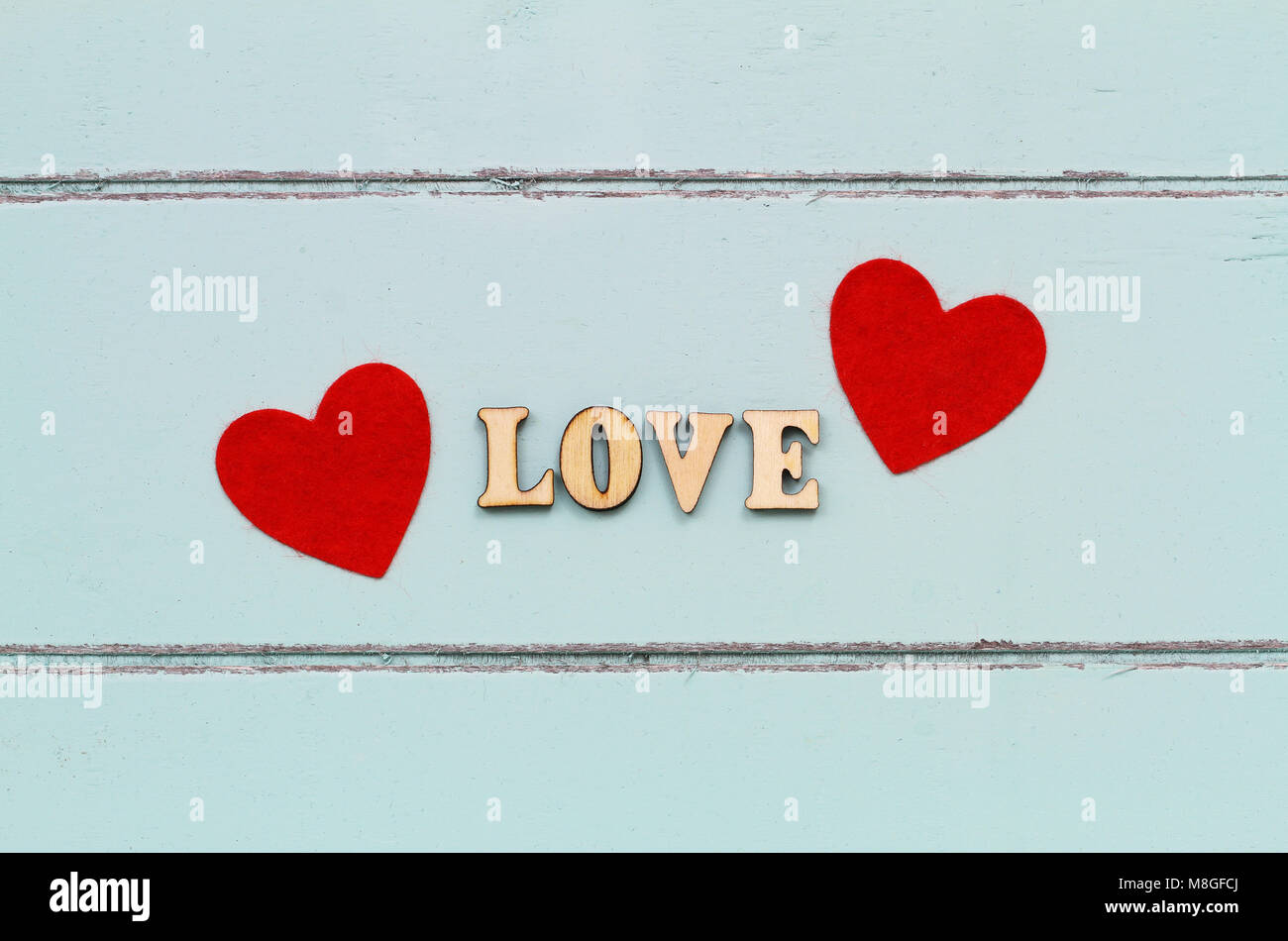 Amore scritte con lettere in legno e due cuori rossi su una superficie di legno Foto Stock