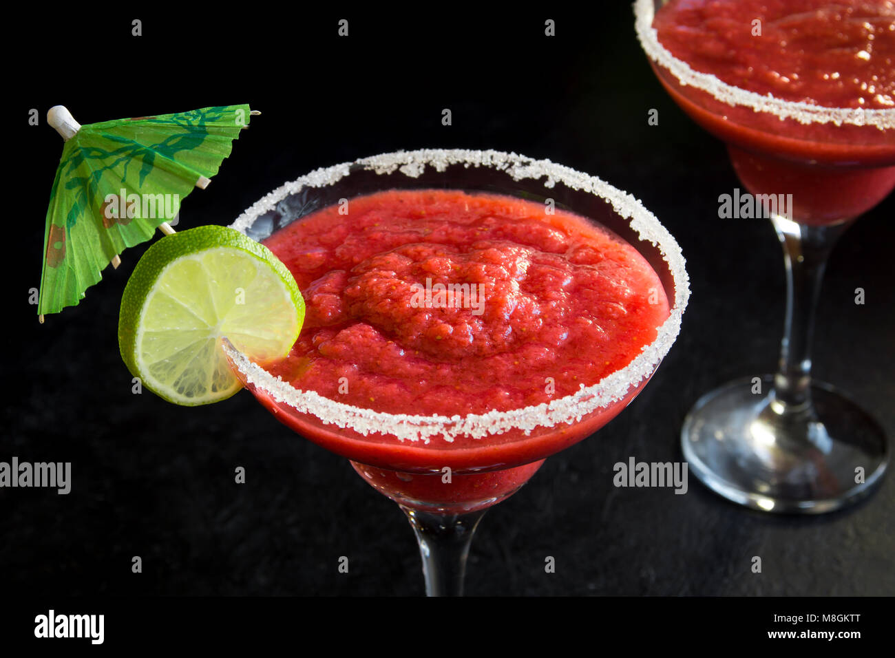 Strawberry Margarita Сocktail con calce su nero tavolo di pietra, copia dello spazio. Congelati o Margarita Daiquiry Cocktail. Foto Stock