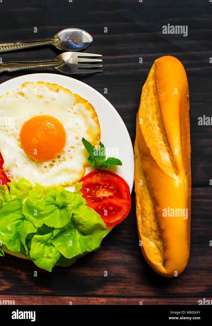 La prima colazione con pane, uova fritte e verdure e pomodoro fritto pezzi su uno sfondo di legno Foto Stock