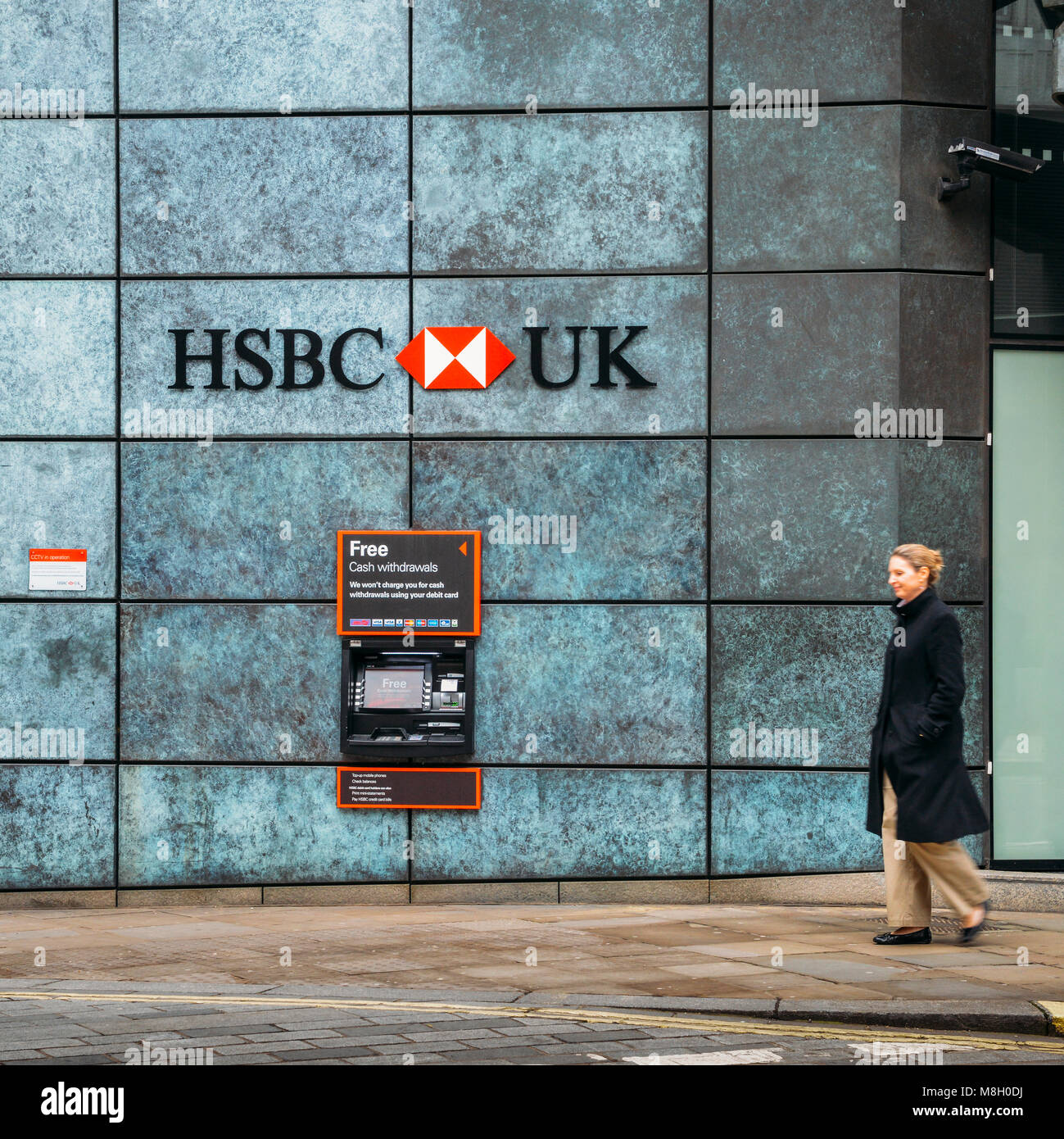 Londra, UK- Mar 13, 2018: donna di mezza età cammina passato un Bancomat dalla banca HSBC pubblicità il prelievo gratuito di denaro contante Foto Stock