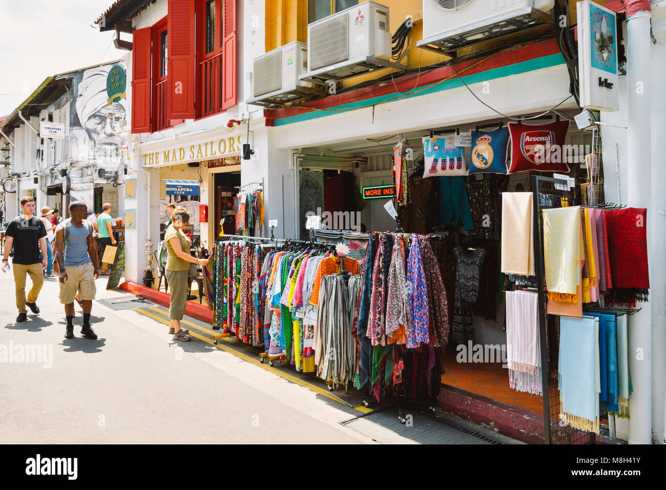 Singapore Haji Lane. Tra il pre-guerra in stile coloniale botteghe, un turista esplora un rack di colorate in stile arabo di abbigliamento. Foto Stock