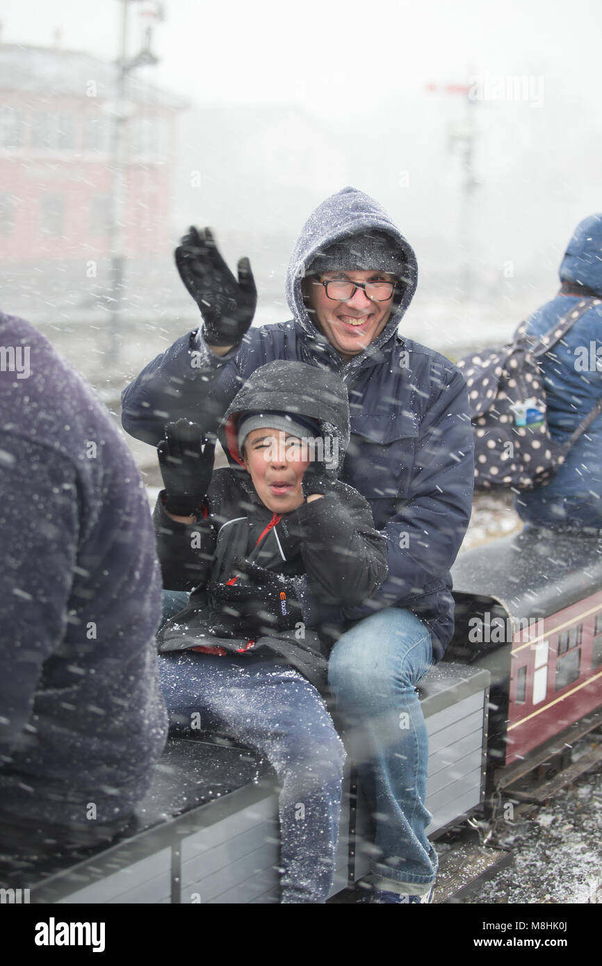 Kidderminster, Regno Unito. 17th marzo 2018. Tempo nel Regno Unito: Mentre la Ferrovia della Severn Valley celebra il successo del 'Weekend di Gala di Festa', gli appassionati di treno di tutte le età sperimentano temporaneamente le condizioni di Blizzard durante tutta la giornata. Nonostante il forte, freddo amaramente, venti est che portano ad un significativo vento freddo, nulla ferma gli appassionati di ferrovia (di tutte le età!) godendo di un giro in treno. Una famiglia britannica viene catturata all'aperto in una neve d'inverno Blizzard, in sella a un treno in miniatura! Credito: Lee Hudson/Alamy Live News Foto Stock