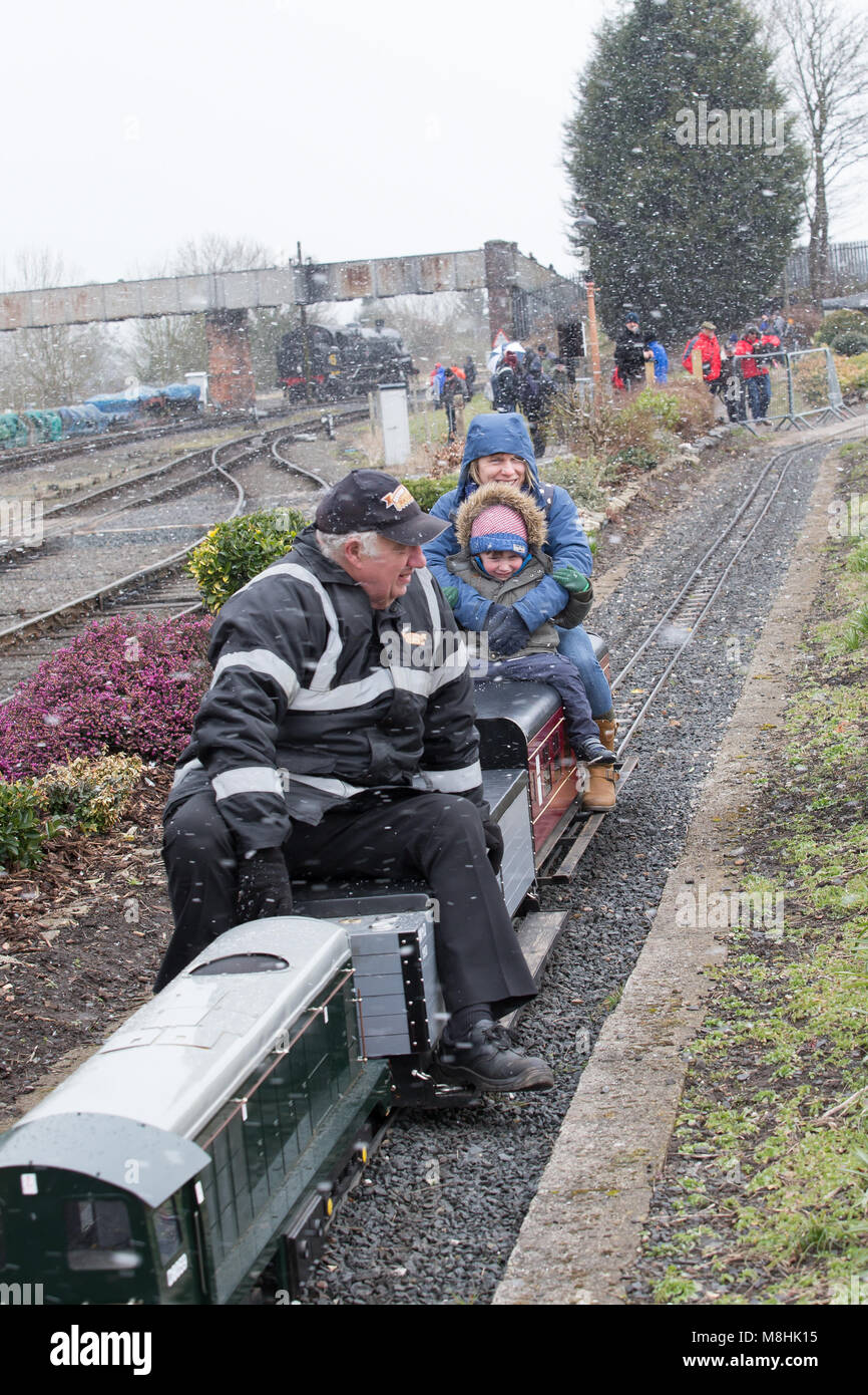 Kidderminster, Regno Unito. 17th marzo 2018. Tempo nel Regno Unito: Mentre la Ferrovia della Severn Valley celebra il successo del 'Weekend di Gala di Festa', gli appassionati di treno di tutte le età sperimentano temporaneamente le condizioni di Blizzard durante tutta la giornata. Nonostante il forte, freddo amaramente, venti est che portano ad un significativo vento freddo, nulla ferma gli appassionati di ferrovia (di tutte le età!) godendo di un giro in treno. Una famiglia britannica viene catturata all'aperto in una neve d'inverno Blizzard, in sella a un treno in miniatura! Credito: Lee Hudson/Alamy Live News Foto Stock
