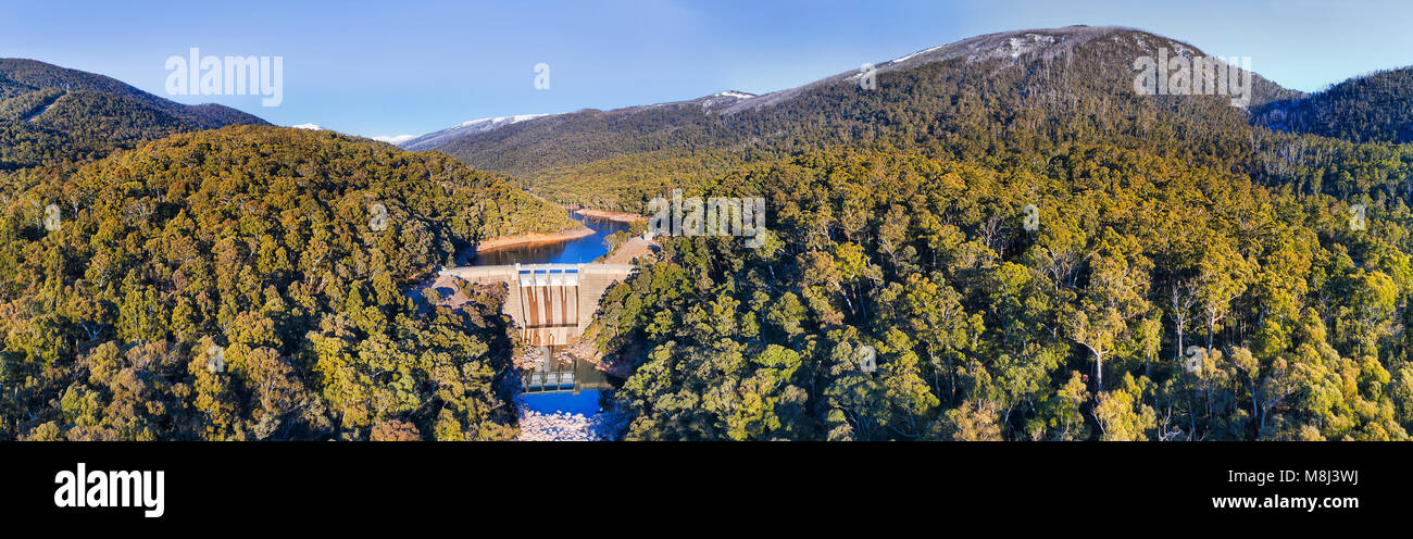 Antenna di ampio panorama sulla diga Guthega nelle montagne innevate sul fiume nevoso durante la stagione invernale con lontane cime dei monti coperti di neve. Foto Stock