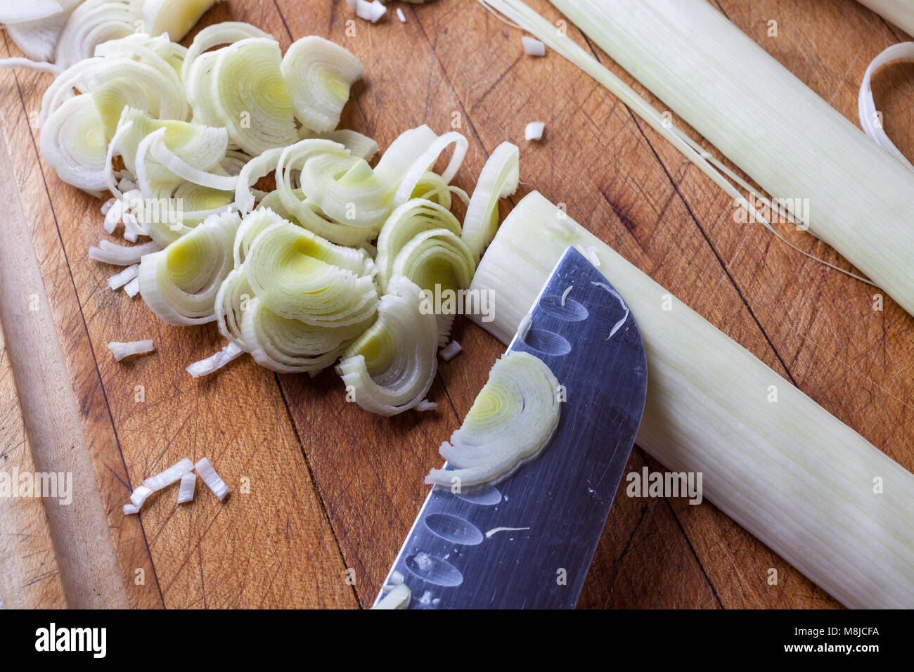 Taglio di porri freschi fette di processo sul tagliere di legno con il coltello Foto Stock