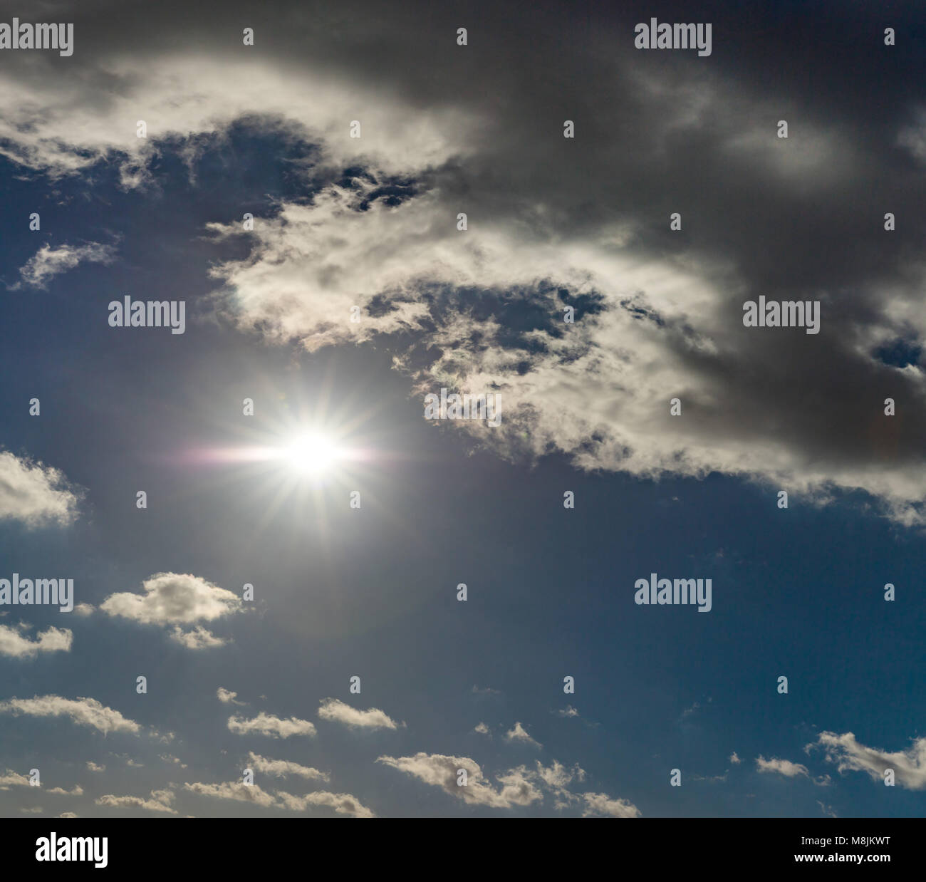 Sole splendente nel cielo blu con nuvole scure Foto Stock
