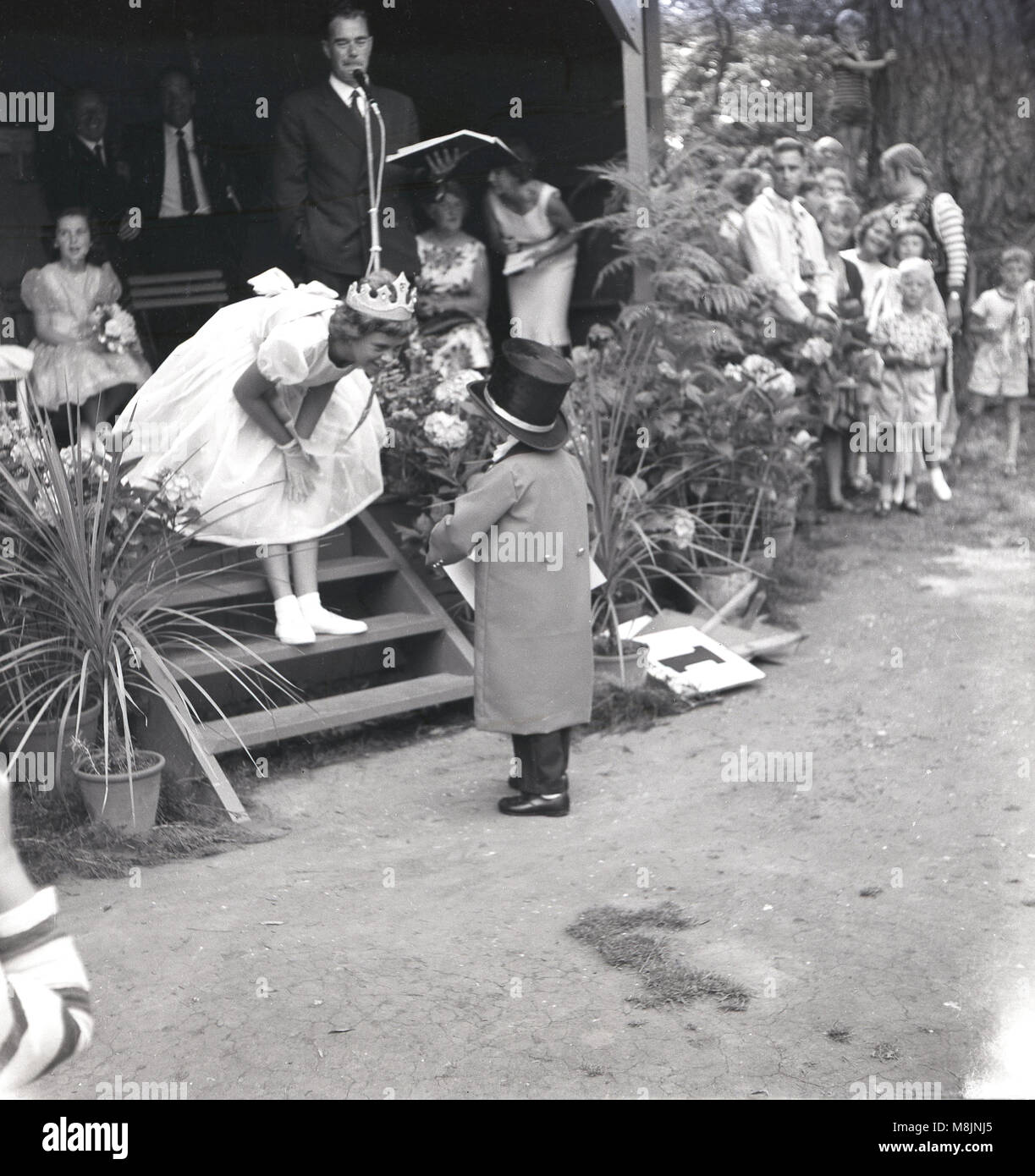 Degli anni Cinquanta, un ragazzino di prendere parte a una fancy dress costume parla di una ragazza vestita come la regina in un ampio mantello e una corona, stando in piedi sui gradini della capanna di giudici, Inghilterra, Regno Unito. Foto Stock