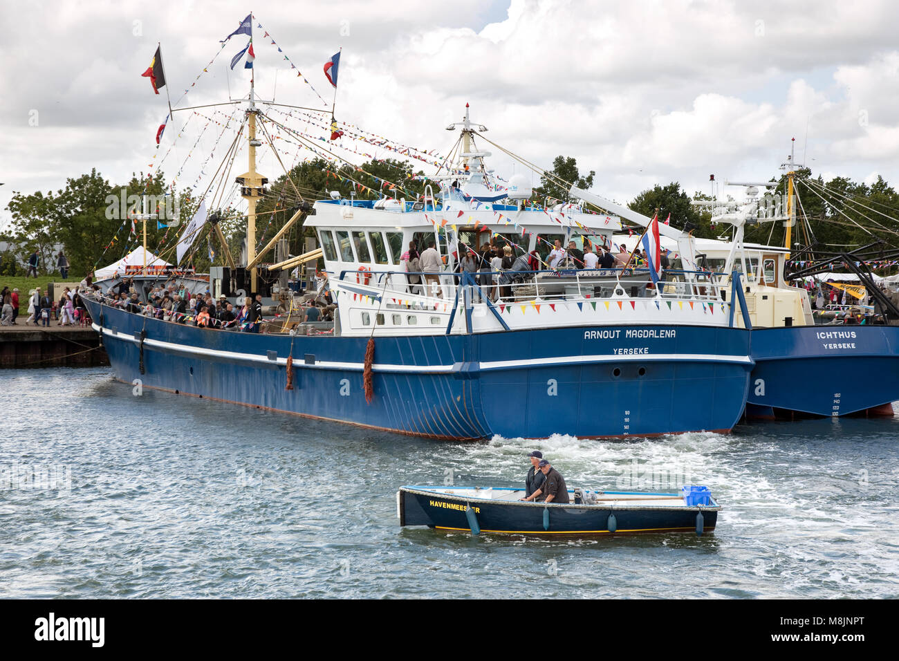 La Capitaneria di porto di vele in una piccola barca dietro una barca da pesca nel porto Foto Stock