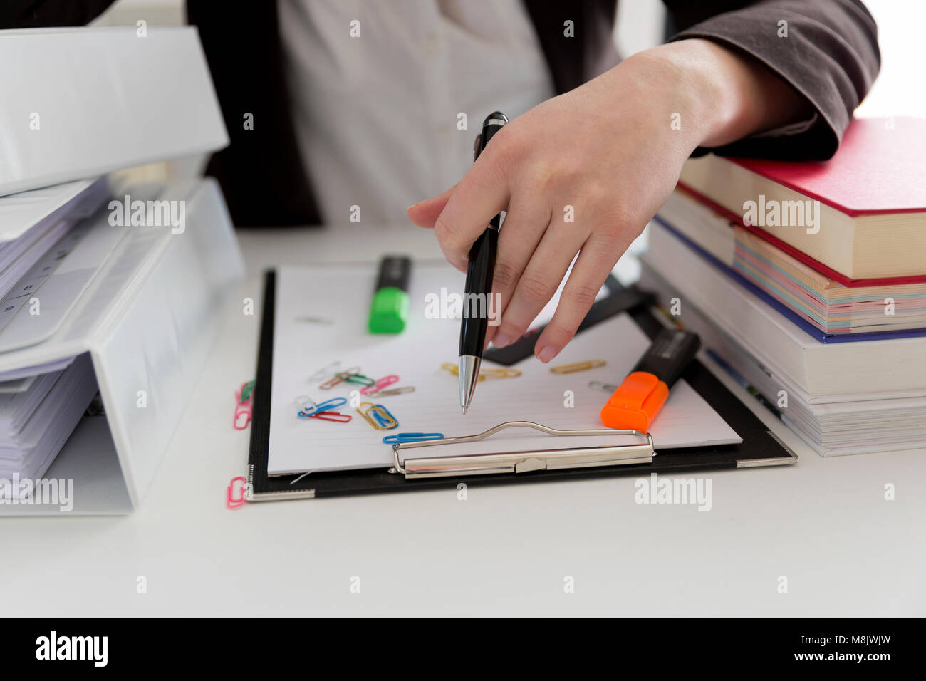 Donna seduta al tavolo pieno di scartoffie, libri, file. Posto di lavoro disordinati. Il sovraccarico e superlavoro Foto Stock