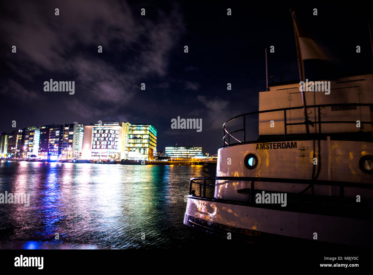 Una vista notturna di Amsterdam canal, con le luci della città e alcune barche vivente Foto Stock
