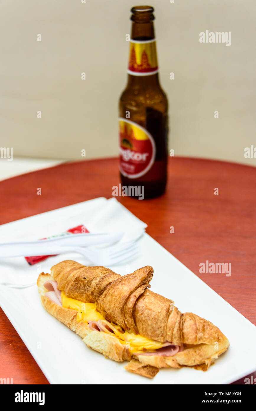 Croissant con prosciutto e formaggio fuso con una bottiglia di birra di Angkor. Foto Stock