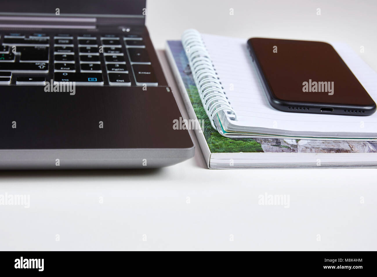 Computer portatile con il telefono cellulare che giace su di una cartella di lavoro di carta su un tavolo bianco - con uno sfondo sfocato Foto Stock