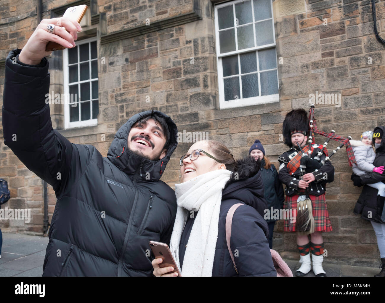 I turisti tenendo selfie con piper musicista di strada sul Royal Mile di Edimburgo Città Vecchia, Scotland, Regno Unito Foto Stock