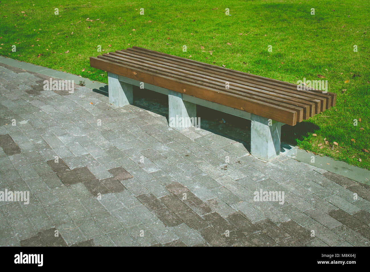 In legno banco lungo l'impostazione concreta sul marciapiede accanto a erba verde prato campo a parco pubblico. Foto Stock