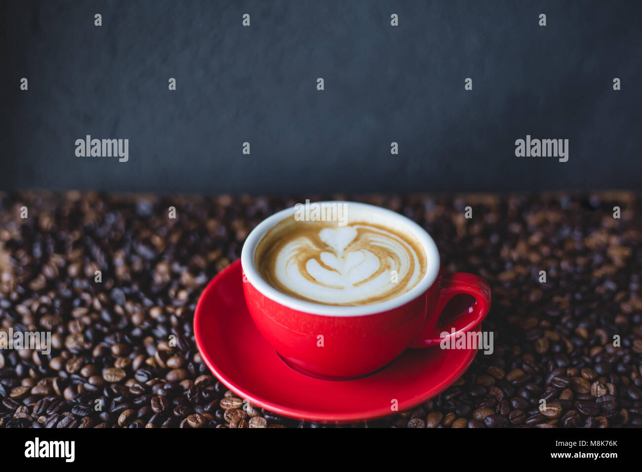 Un rosso tazza di caffè con latte sul chicco di caffè con sfondo di pietra Foto Stock