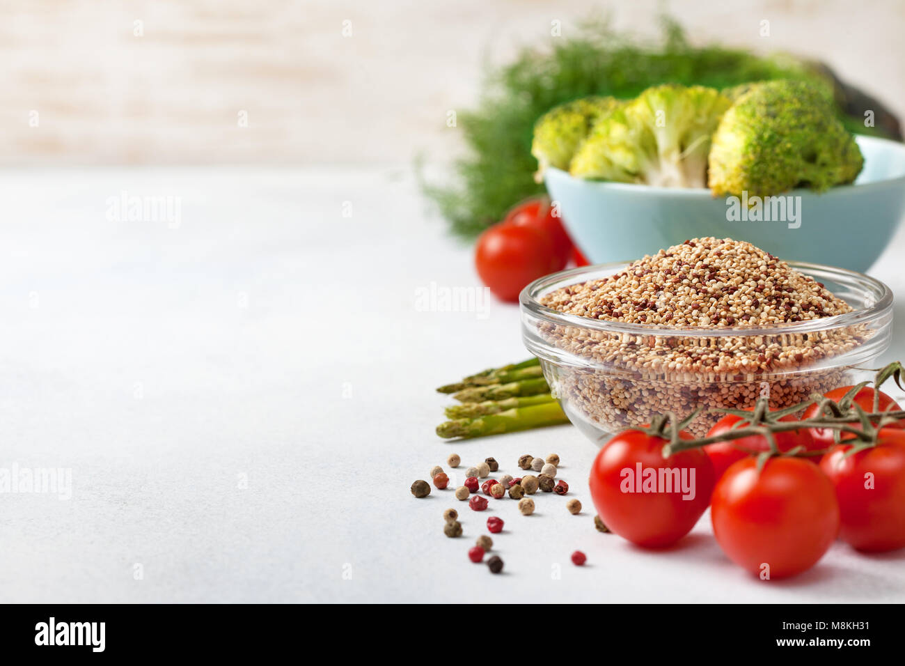 Una sana dieta alimentare. la quinoa in una ciotola di vetro, pomodori ciliegini, asparagi, broccoli su uno sfondo luminoso calcestruzzo Foto Stock