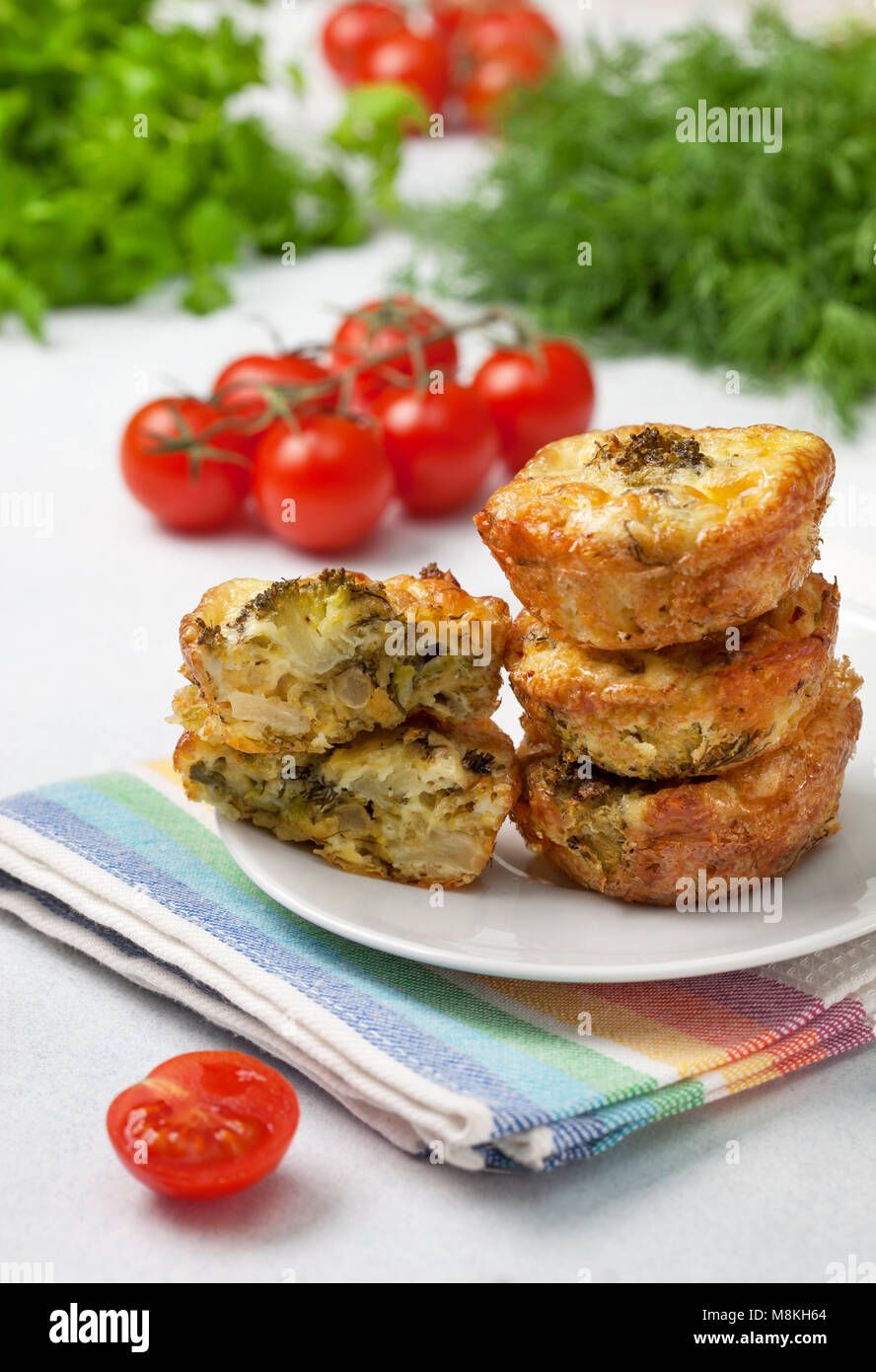 Una sana prima colazione. broccoli morsi di formaggio (Muffin), pomodori freschi, erbe fresche sul calcestruzzo leggero sfondo Foto Stock