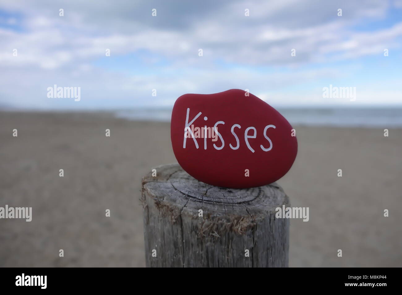 Baci il testo su un rosso pietra dipinta su un palo di legno e lo sfondo di spiaggia Foto Stock