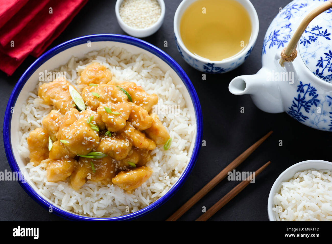 Asian di sesamo o di pollo teriyaki con il riso nel recipiente, il tè verde e bastoncini su sfondo scuro. Vista superiore Foto Stock