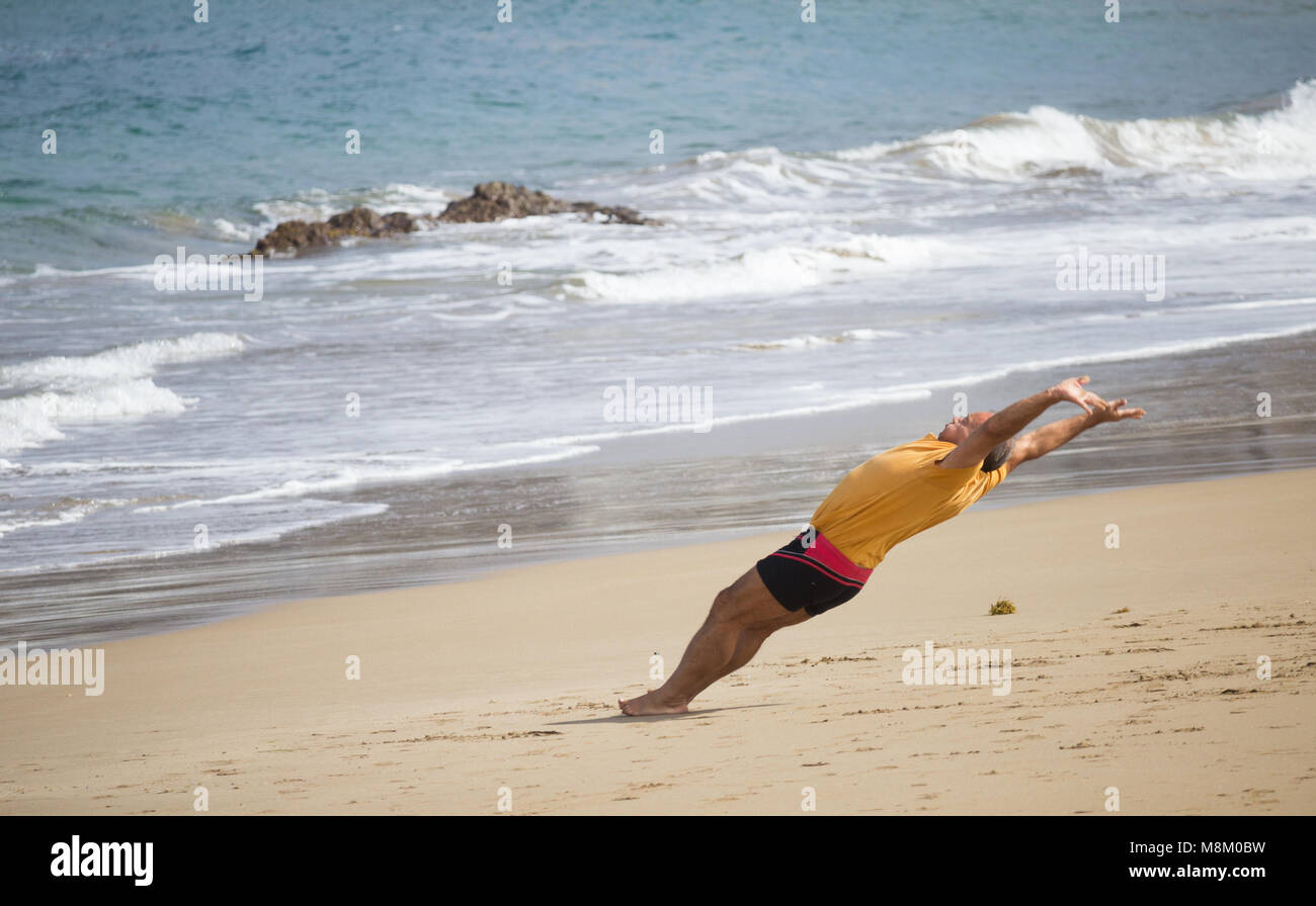 Un uomo sembra essere sfidando la gravità come egli è fotografato metà capriola su una spiaggia in Spagna. Foto Stock