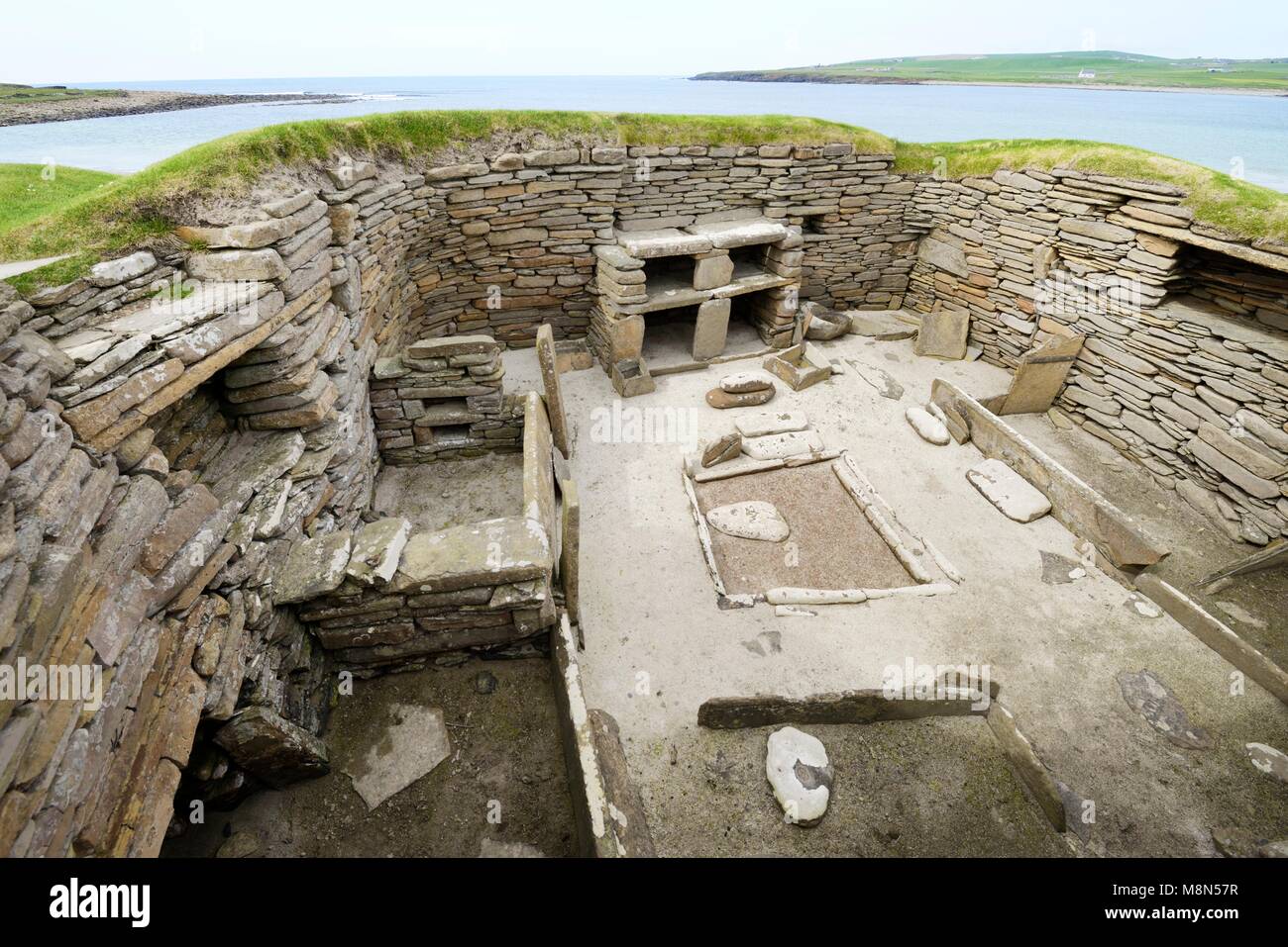 Skara Brae Età della pietra villaggio neolitico di Skaill, isole Orcadi, Scozia. Interno scatola, letti, focolare e comò 3100 BC. Casa 1 con la baia di Skaill dietro Foto Stock