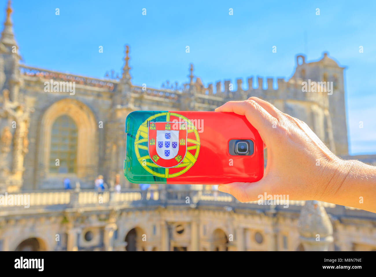 Turismo e concetto di viaggio in Portogallo. Chiusura del telefono cellulare con la bandiera del Portogallo il coperchio di scattare le foto di località turistica in città templare. Convento di Cristo o fortezza dei Templari su sfondo sfocato. Foto Stock