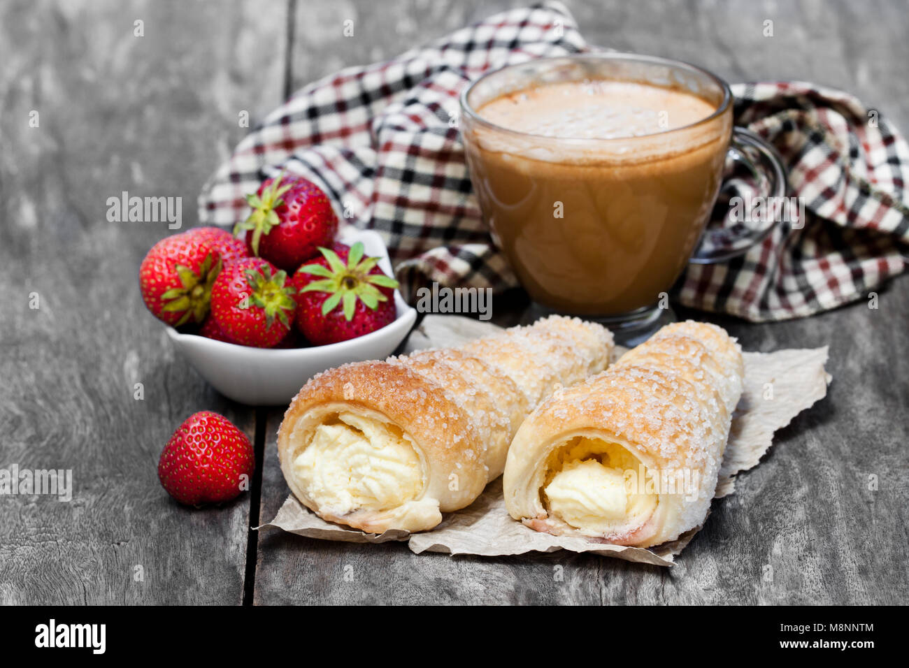 Pasta sfoglia le corna con tazza di cappuccino e fragola sul tavolo di legno Foto Stock