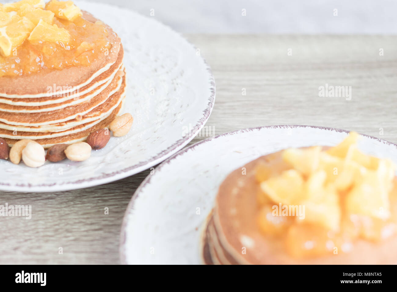 2 bianco piastre modellato con frittelle e marmellata di arancia e i dadi sul tavolo di legno dello sfondo. Primo piano. Copyspace Foto Stock
