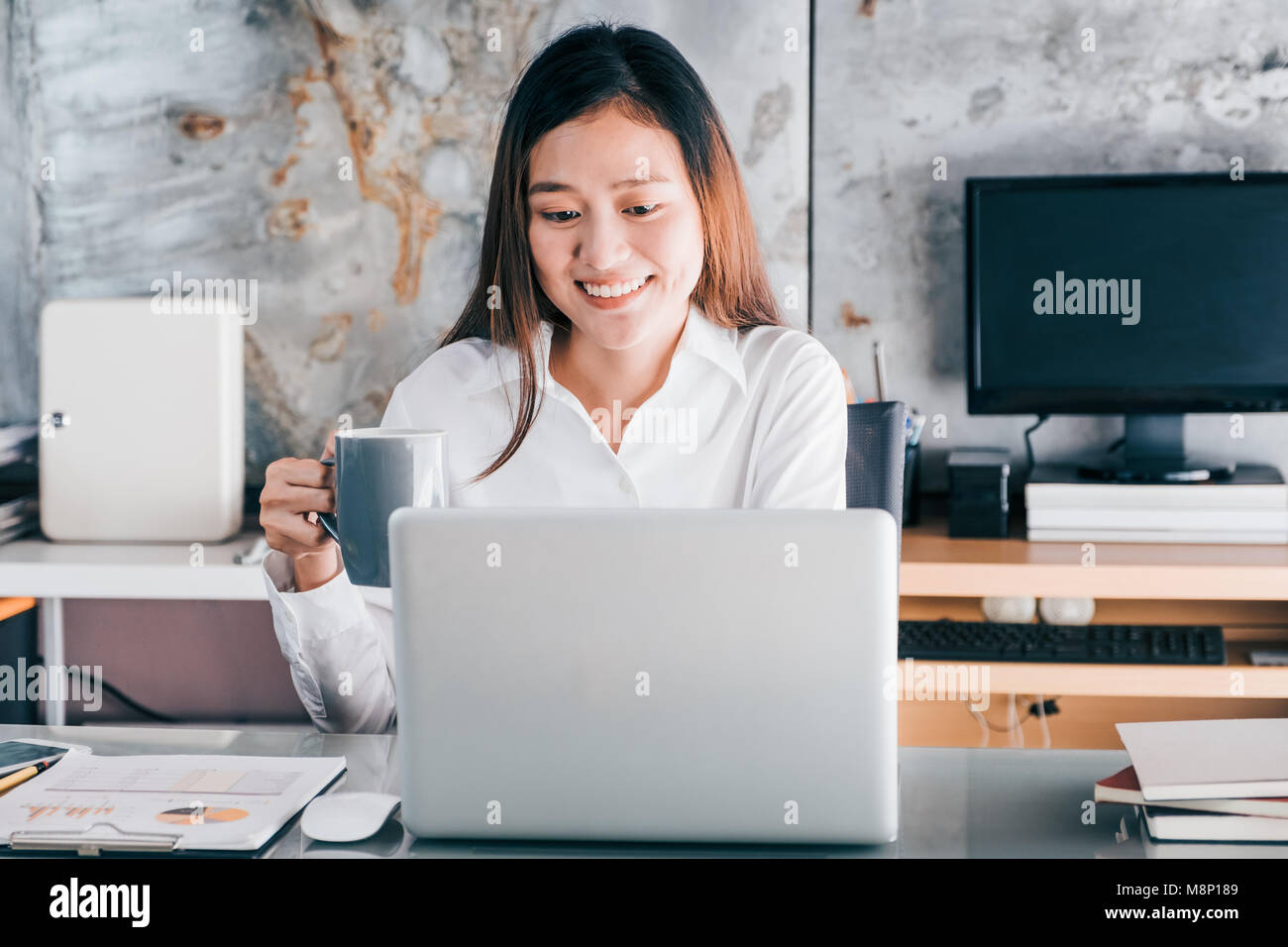 Imprenditrice asiatici prendere una pausa caffè dopo il lavoro al computer laptop sulla scrivania con volto sorridente,felice vita in ufficio concetto,donna lavoratrice in moderni h Foto Stock