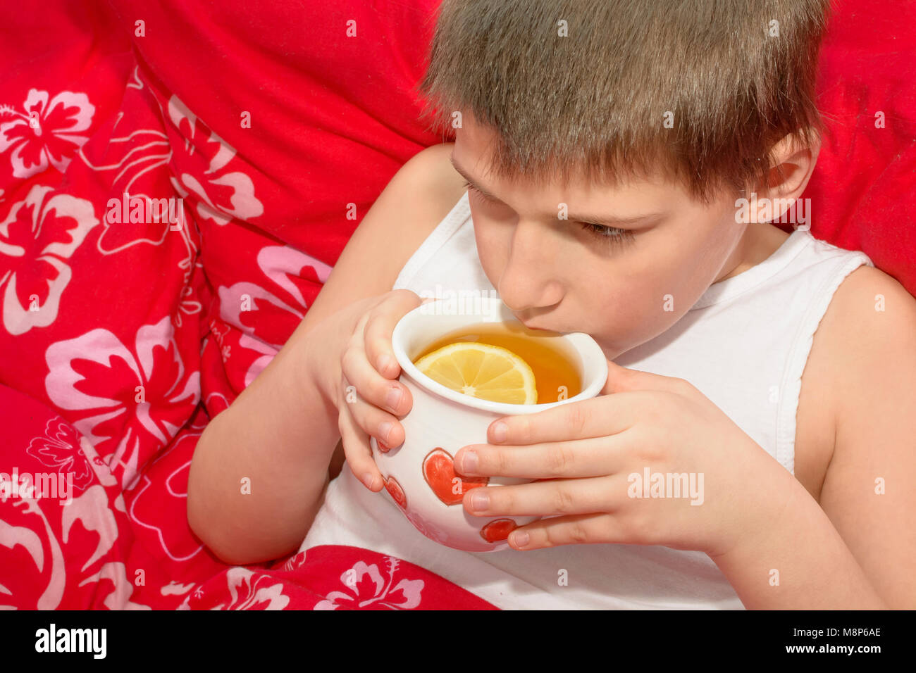 Un ragazzo malato tenendo un bicchiere con un caldo tè al limone. La stagione influenzale. Un ragazzo malato bevande di tè caldo con limone. Foto Stock