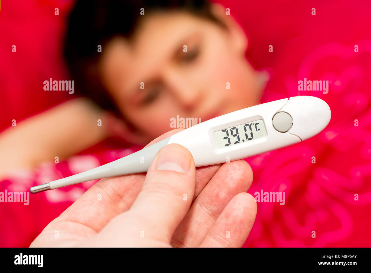 Un ragazzo malato giacente in letto. La stagione influenzale. Viene visualizzata la temperatura sul termometro. Una mano che tiene un termometro. Foto Stock