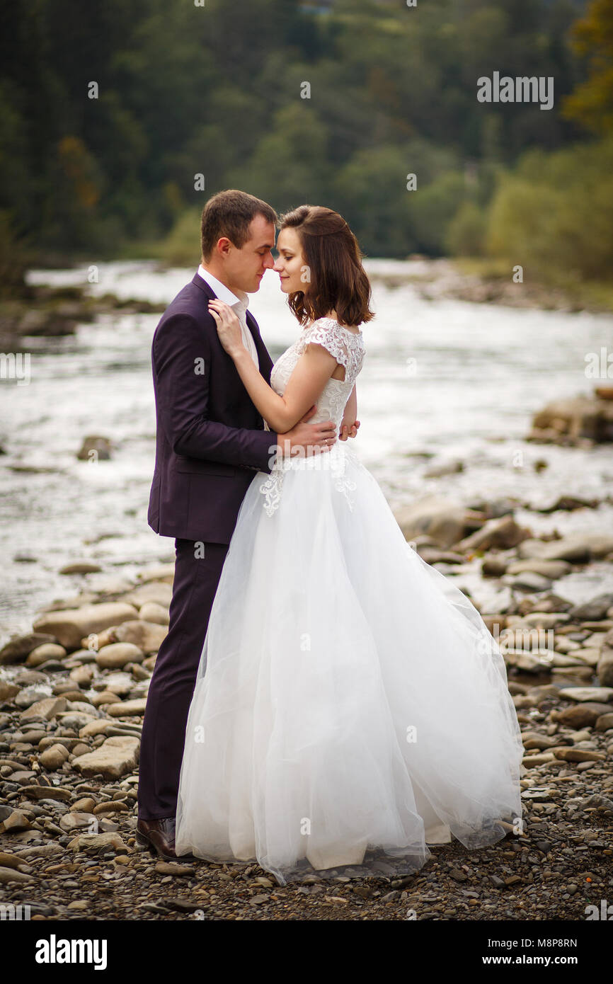 Happy sposi in piedi e sorridente sulla riva del fiume Foto Stock