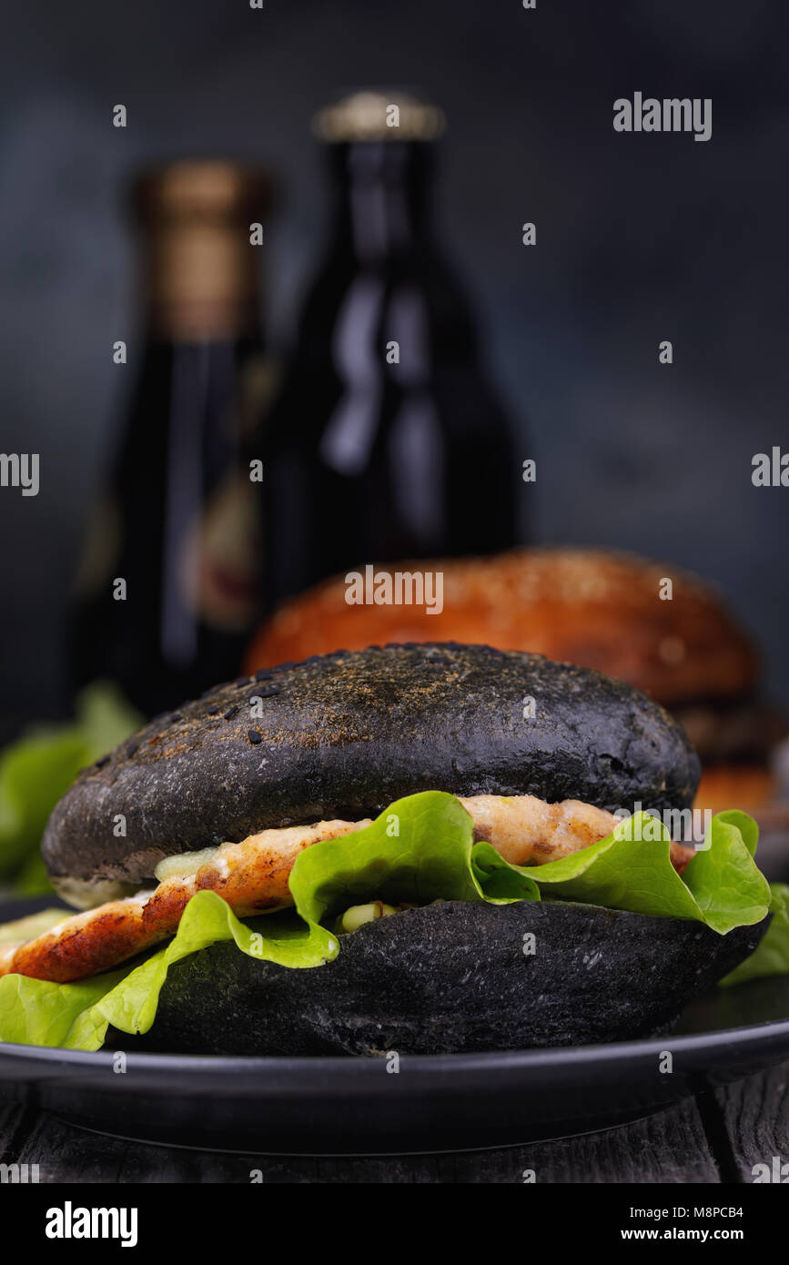 Cucinata fresca hamburger con rotolo di colore nero, verdure e salmone cotoletta. Sandwich fatti in casa da vicino Foto Stock