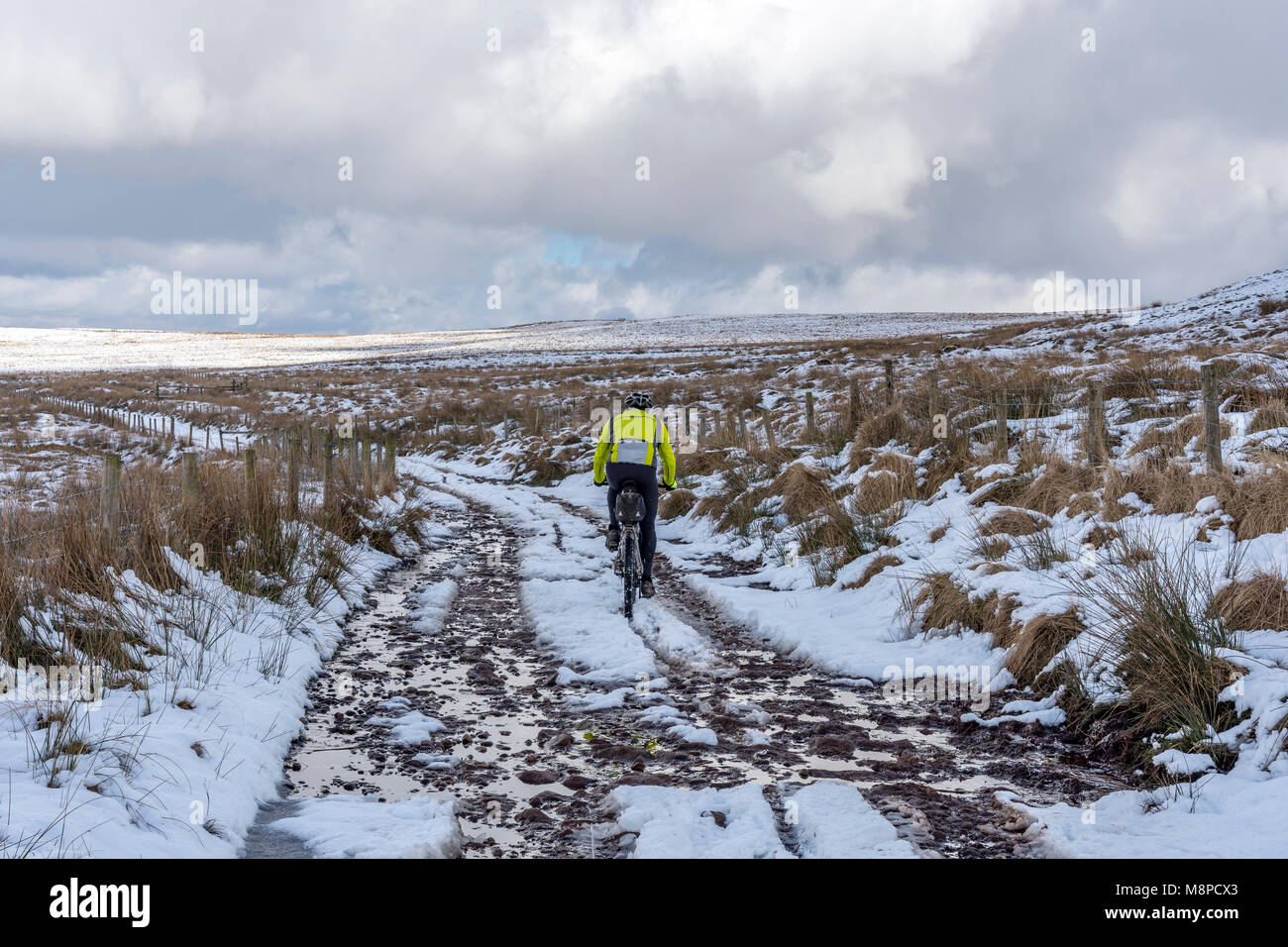 Un lone mountain bike ciclista fa il suo modo proprio di fronte all'alborella Lancashire Moorland REGNO UNITO attraverso la neve e ghiaccio Foto Stock