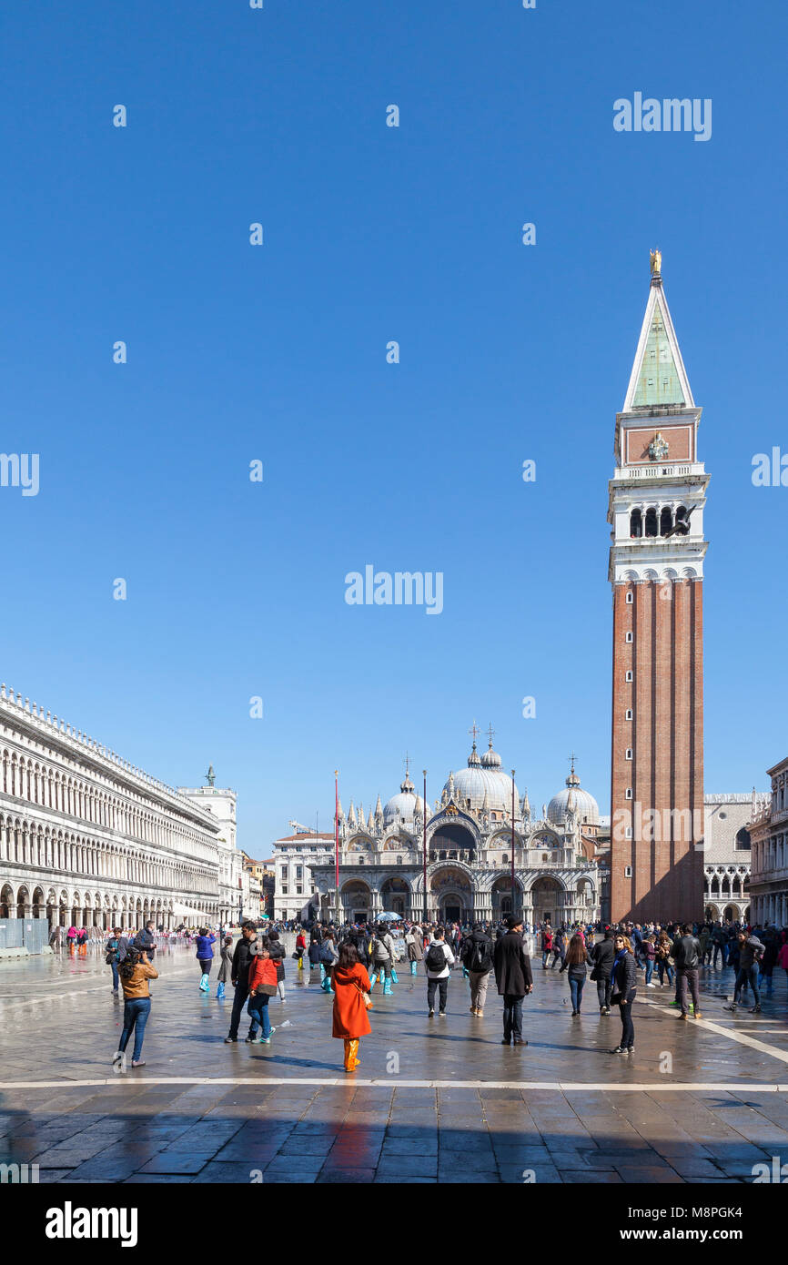 Turisti in Piazza San Marco, Piazza San Marco, dopo acqua alta con molti indossando colorato in plastica sopra le scarpe, Venezia, Veneto, Italia su un soleggiato ble s Foto Stock