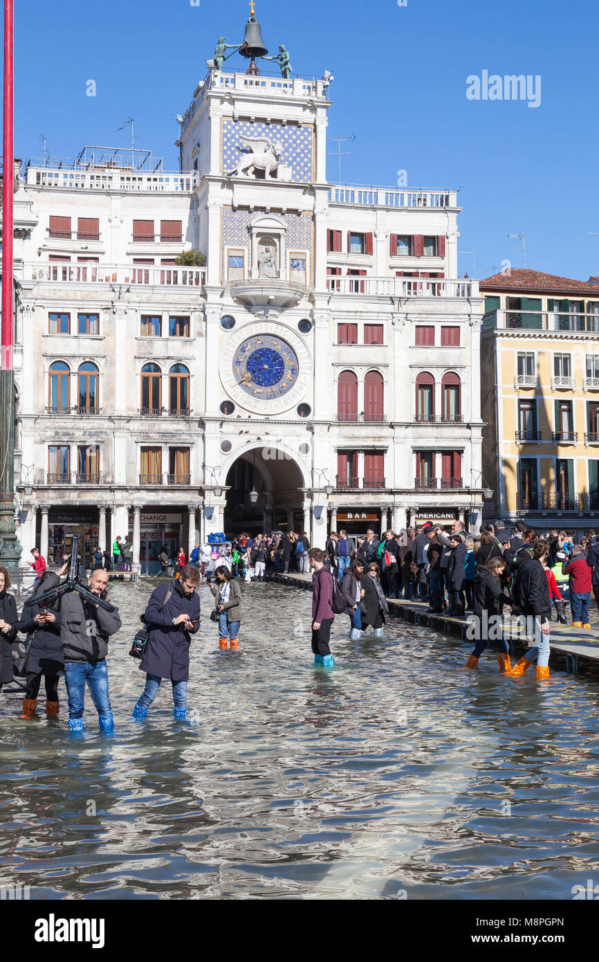 I turisti guadare attraverso Acqua Alta inondazioni in Piazza San Marco, Piazza San Marco, di fronte alla Torre dell Orologio, Venezia, Italia Foto Stock