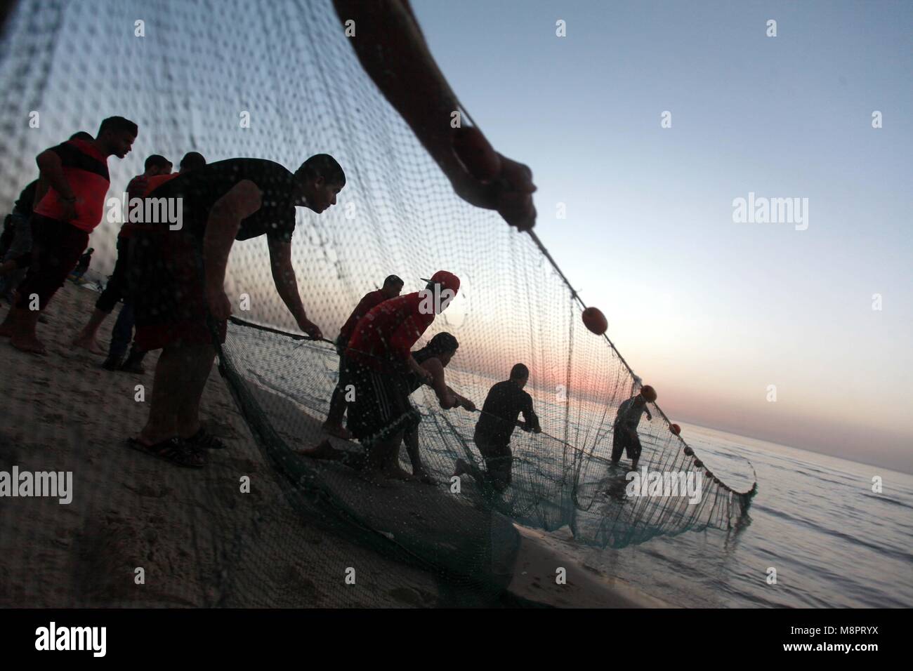 La città di Gaza, Striscia di Gaza, Territori palestinesi. Xix Mar, 2018. I pescatori palestinesi tirare fuori le loro reti da acqua a la spiaggia di Gaza City durante il tramonto su Marzo 19, 2018 Credit: Yasser Qudih APA/images/ZUMA filo/Alamy Live News Foto Stock